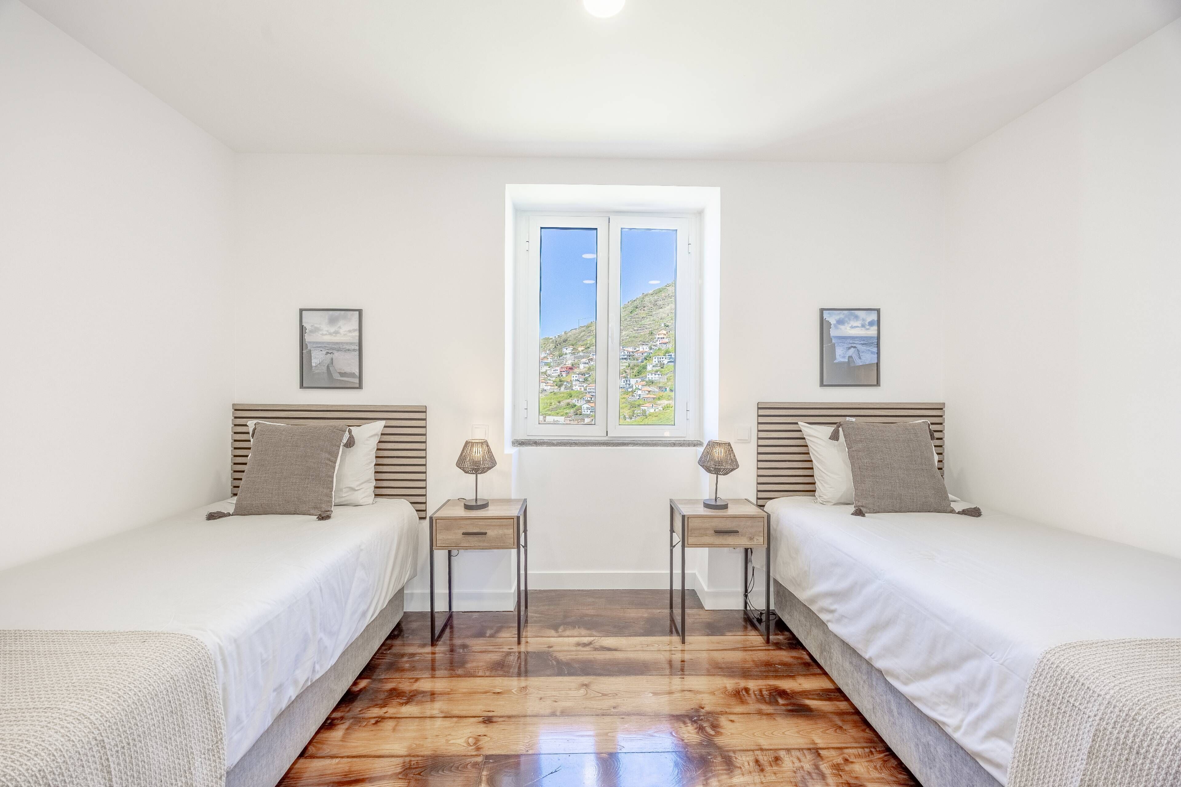 Une chambre avec deux lits simples, une fenêtre donnant sur des maisons et un plancher en bois.