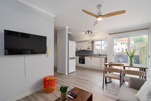 A modern kitchen with white cabinets, a built-in oven, and a dining area with a table and chairs. - MJ - North Escape by YOUR KEY (Porto Moniz)