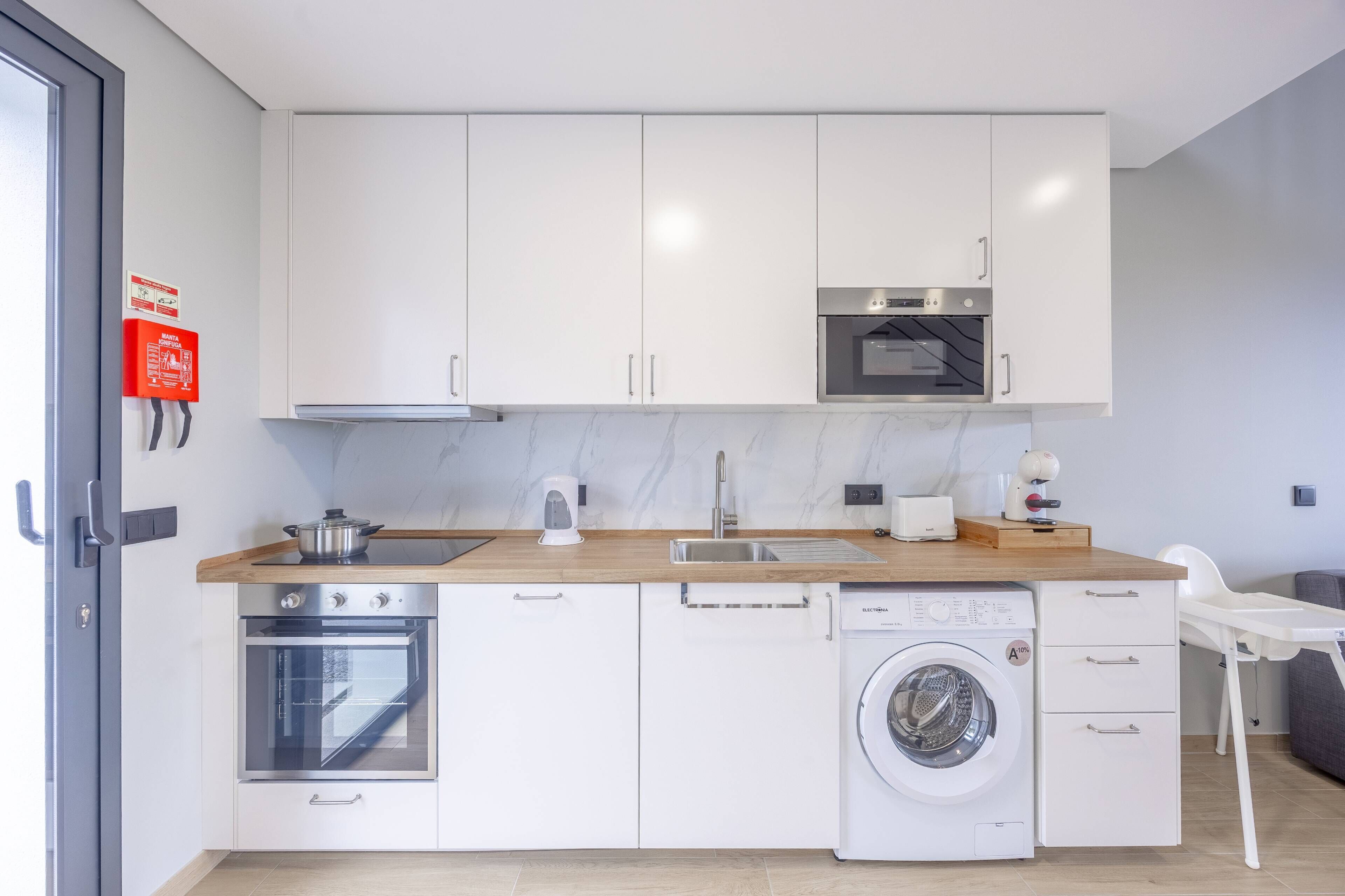Eine moderne Küche mit weißen Schränken, einem Backofen, einer Mikrowelle, einem Spülbecken und einer Waschmaschine.