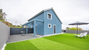 Ein modernes Haus mit blauer Fassade, einer überdachten Terrasse und einem gepflegten Rasen.