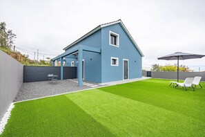 Ett modernt hus med en blå fasad, en täckt uteplats och en välskött gräsmatta.