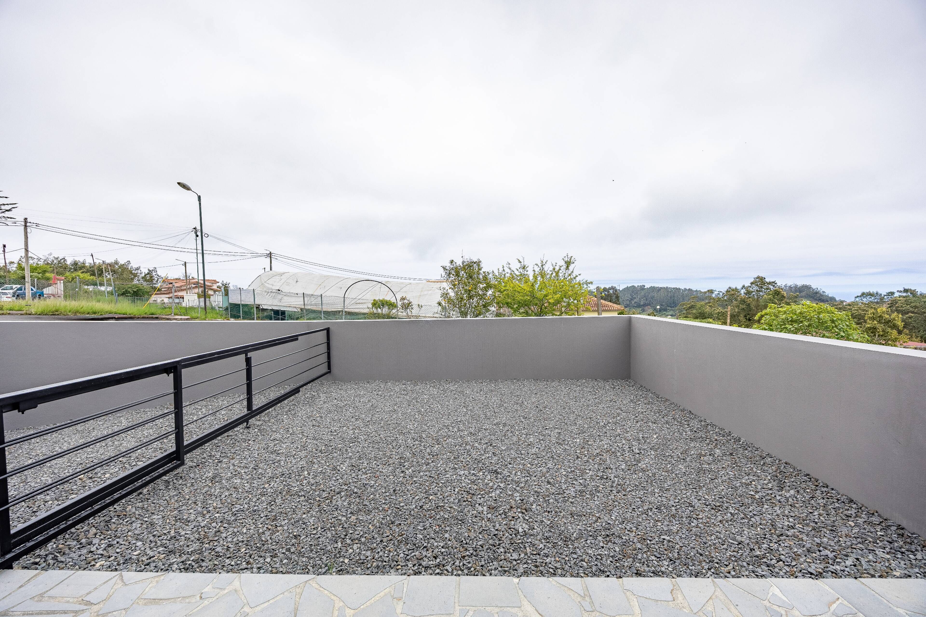 Una terraza al aire libre con suelo de grava, barandilla de metal y vista a un campo deportivo.