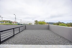 An outdoor terrace with a gravel floor, a metal railing, and a view of a sports field.