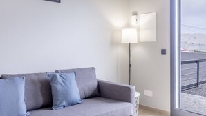 Ein modernes Wohnzimmer mit einem grauen Sofa, zwei Wandleuchten und einem großen Fenster mit Blick auf eine verschneite Landschaft.