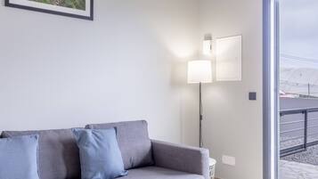 A modern living room with a grey sofa, two wall-mounted lamps, and a large window offering a view of a snowy landscape.