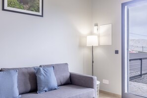 Ett modernt vardagsrum med en grå soffa, två väggmonterade lampor och ett stort fönster med utsikt över ett snötäckt landskap.
