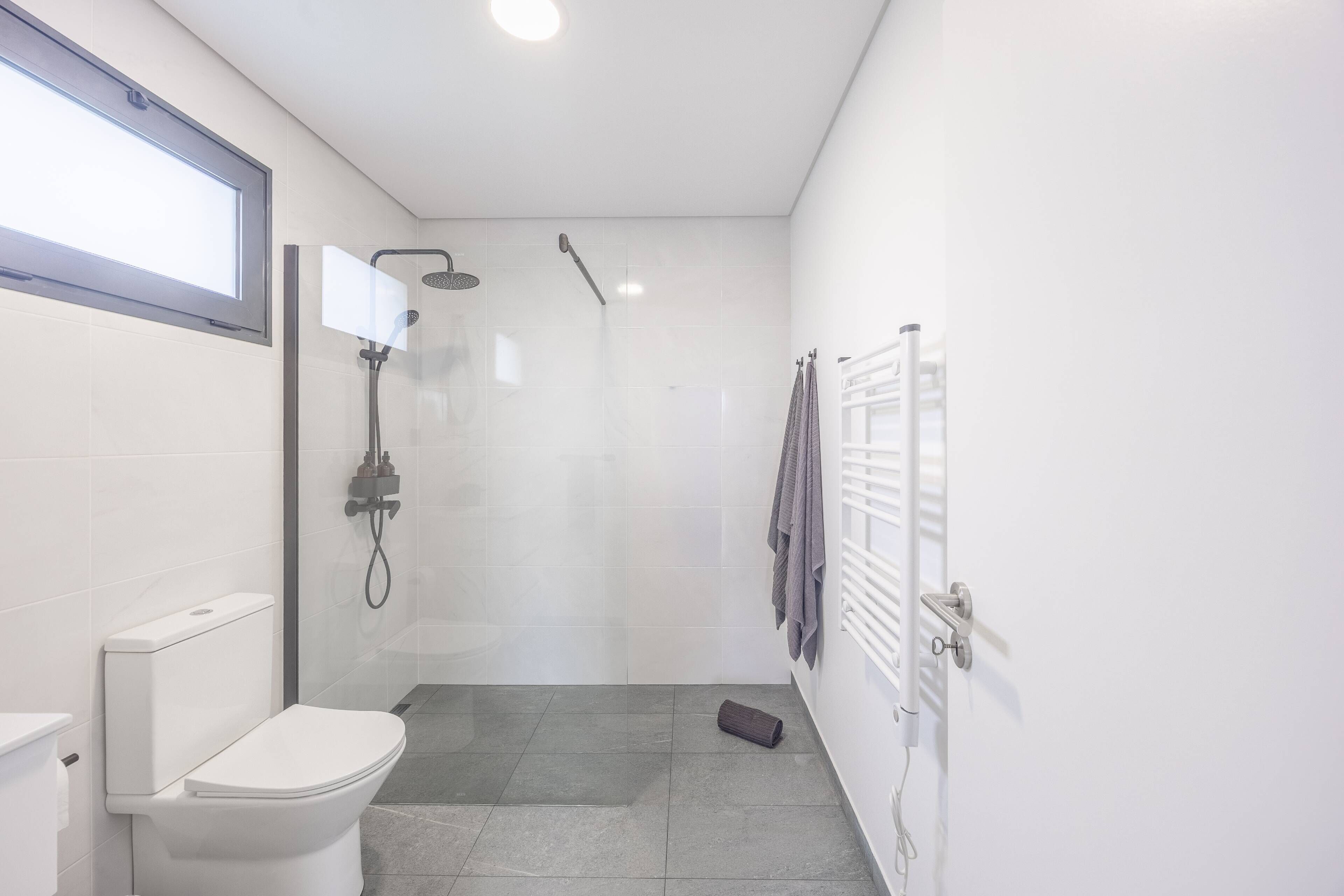 Een compacte, moderne badkamer met toilet, douche en handdoekhouder.