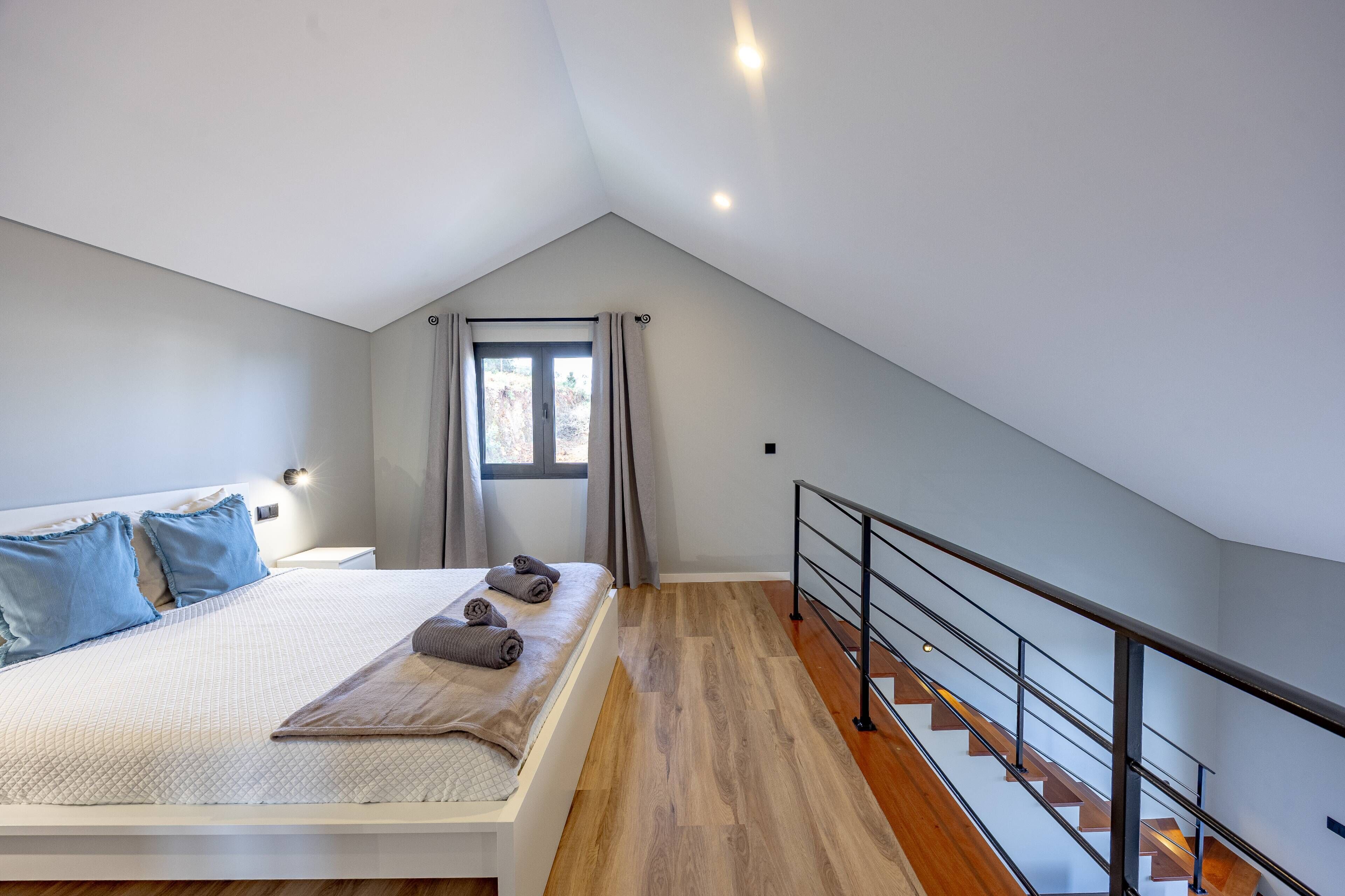 Un dormitorio con cama, almohadas, una ventana y una escalera.