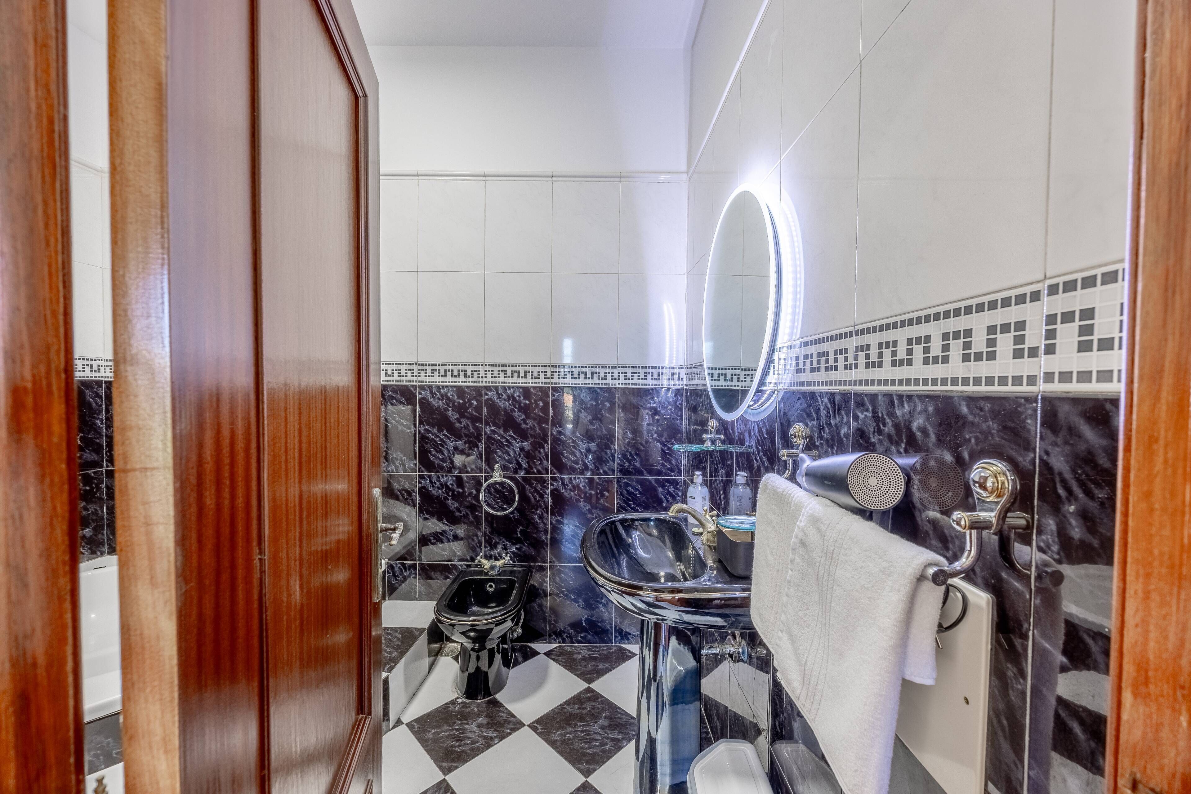 Ein Badezimmer mit einem schwarz-weißen Schachfußboden, einem Spiegel mit Beleuchtung, einem Waschbecken mit Handtuch und einer Duschkabine.