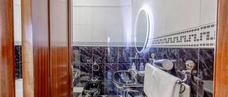 A bathroom with a black and white checkered floor, a mirror with a light, a sink with a towel, and a shower area.