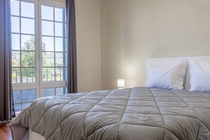 Ein Schlafzimmer mit einem Bett, einem Fenster mit Vorhängen und einem Nachttisch mit Lampe.