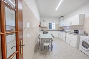 Ett modernt kök med vita skåp, ett matbord med stolar, en inbyggd ugn och en tvättmaskin.