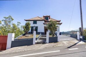 Ein zweistöckiges Haus mit Ziegeldach, einem Hauseingang mit Treppe und einem umzäunten Auffahrt.