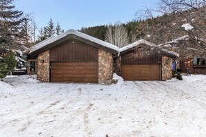 Eine Garage für zwei Autos mit einer Steinfront und einem schneebedeckten Dach, eingebettet in eine verschneite Landschaft mit Bäumen.