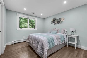 Een slaapkamer met een bed, nachtkastje, wanddecoratie en een raam.