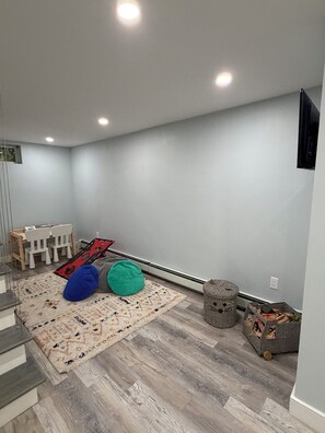 Quarto com escada, área de recreação com tapete e puffs, e cesta com objetos.