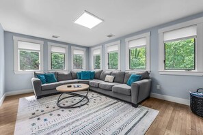 Ein Wohnzimmer mit einem grauen Ecksofa, einem runden Couchtisch und einem gemusterten Teppich.