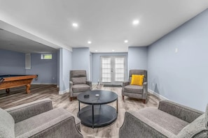 Een moderne woonkamer met een pooltafel, twee fauteuils, een salontafel en een deur die uitkomt op een balkon.