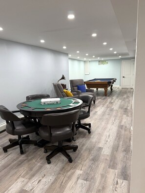 Een kamer met een pooltafel, een pokertafel met groen filz en een biljarttafel.