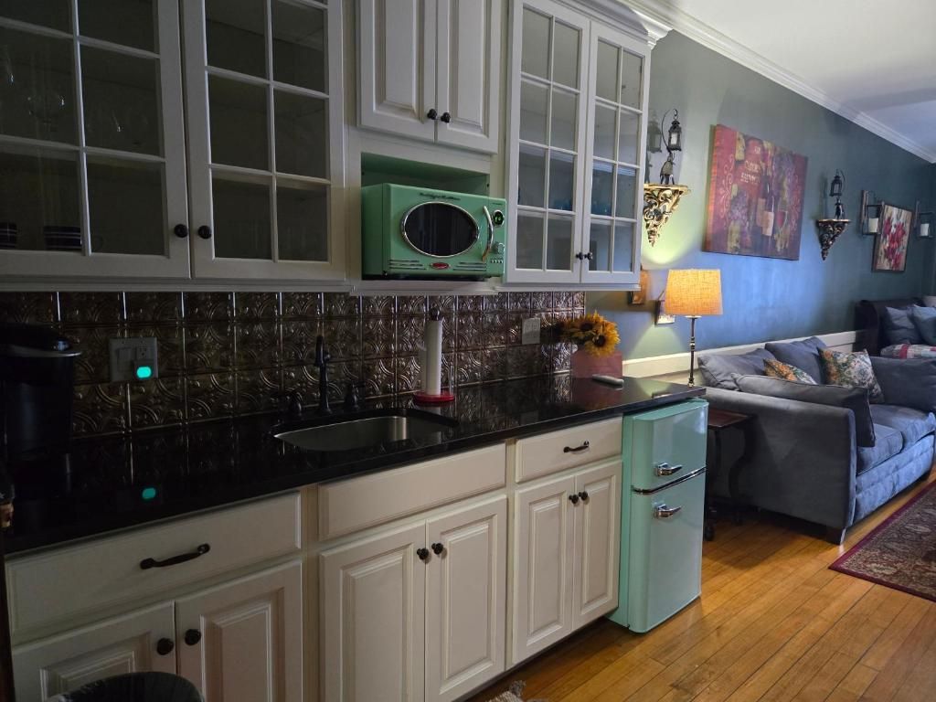A kitchen with white cabinets, a green microwave, and a sink. There is a blue sofa and a rug in the living area.