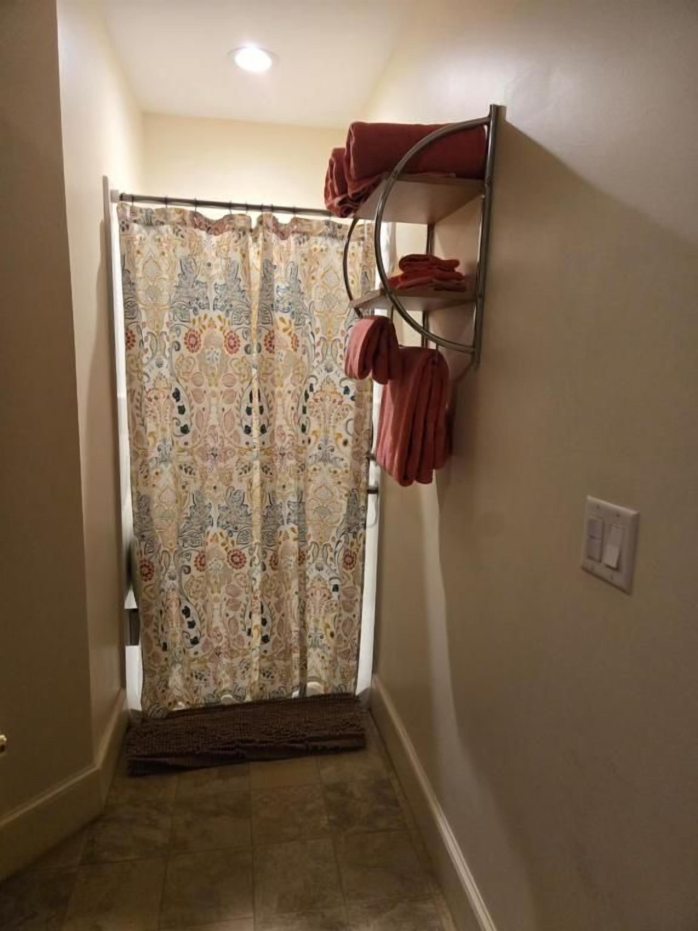 Um banheiro com cortina de chuveiro, porta-toalhas com toalhas, interruptor de luz e porta.