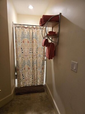 Un baño con cortina de ducha, un perchero con toallas, un interruptor de luz y una puerta.