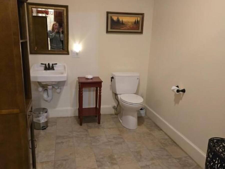 A bathroom with a toilet, sink, mirror, and a small table.