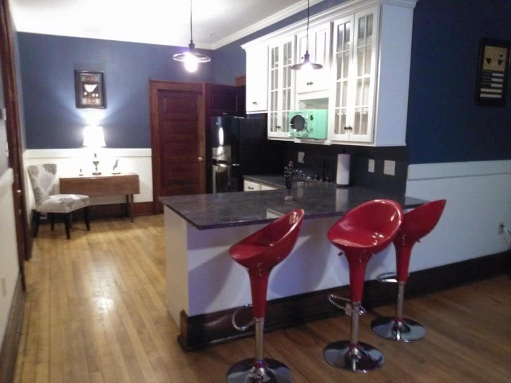 Une cuisine avec un îlot central, deux tabourets de bar rouges, un réfrigérateur et un four à micro-ondes.