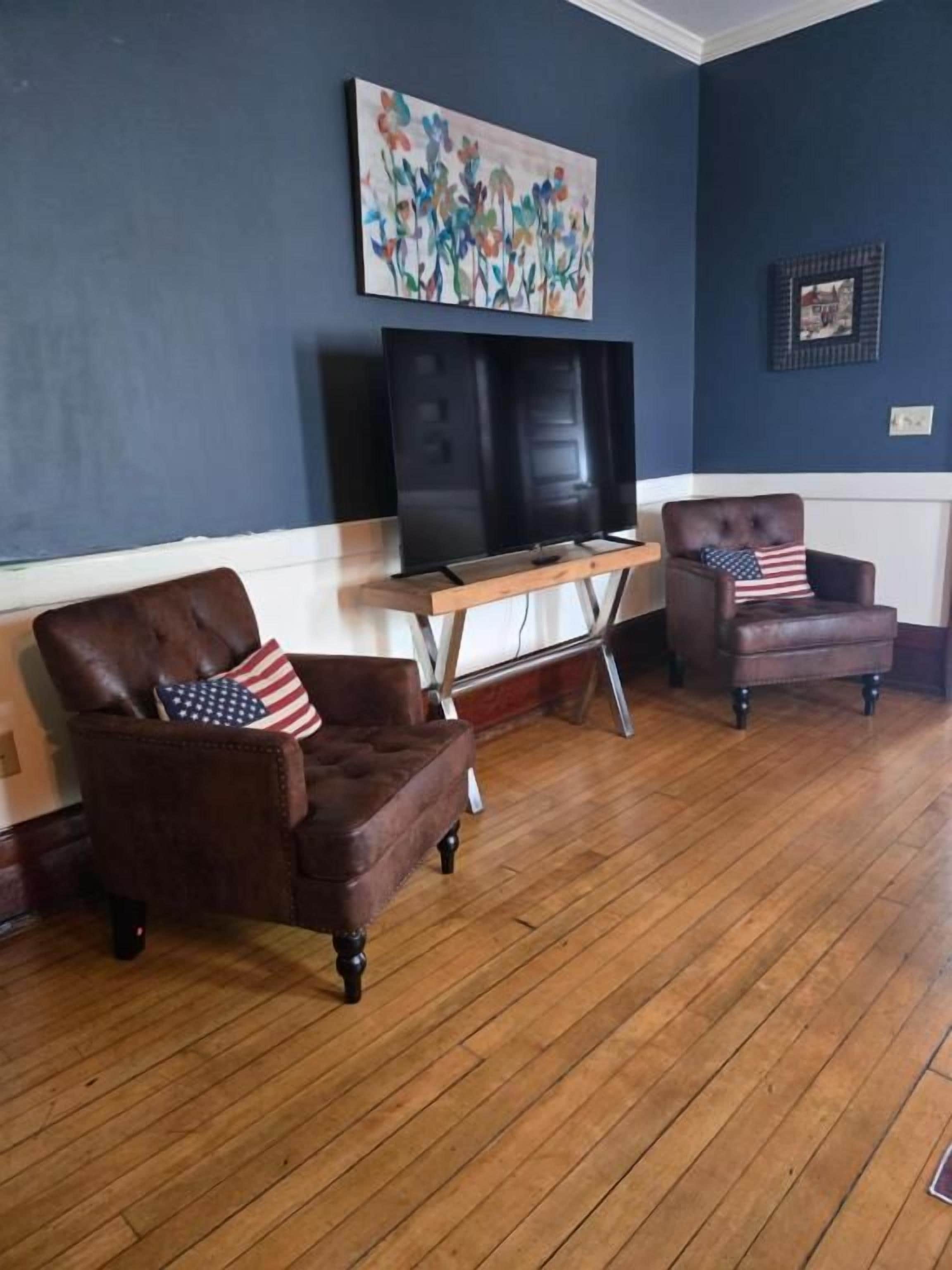 A room with two leather armchairs, a wooden coffee table, and a flat-screen TV on a stand.