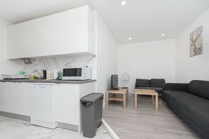 A modern kitchen with white cabinets, a microwave, and a dishwasher. There is a small wooden table with a fan and a gray couch in the living area. - HOUZE City Center spacious 9 rooms flat, best view (Lisboa)