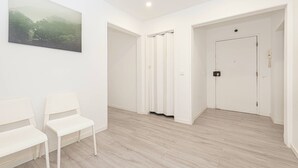 Un corridoio con un quadro, due sedie bianche, una porta e un interruttore della luce.