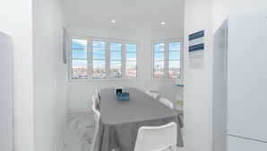 Zona pranzo con tavolo, sedie e vista sulla città attraverso ampie finestre.