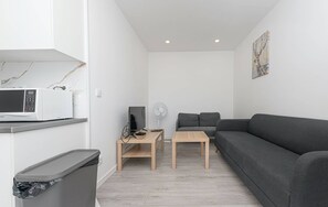 Un espai petit de sala d'estar amb un sofà gris, una taula de centre de fusta, un televisor, un forn microones i un cubell de brossa.