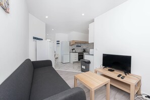 A modern living room with a sofa, a TV on a wooden table, and a kitchen in the background. - HOUZE City Center spacious 9 rooms flat, best view (Lisboa)
