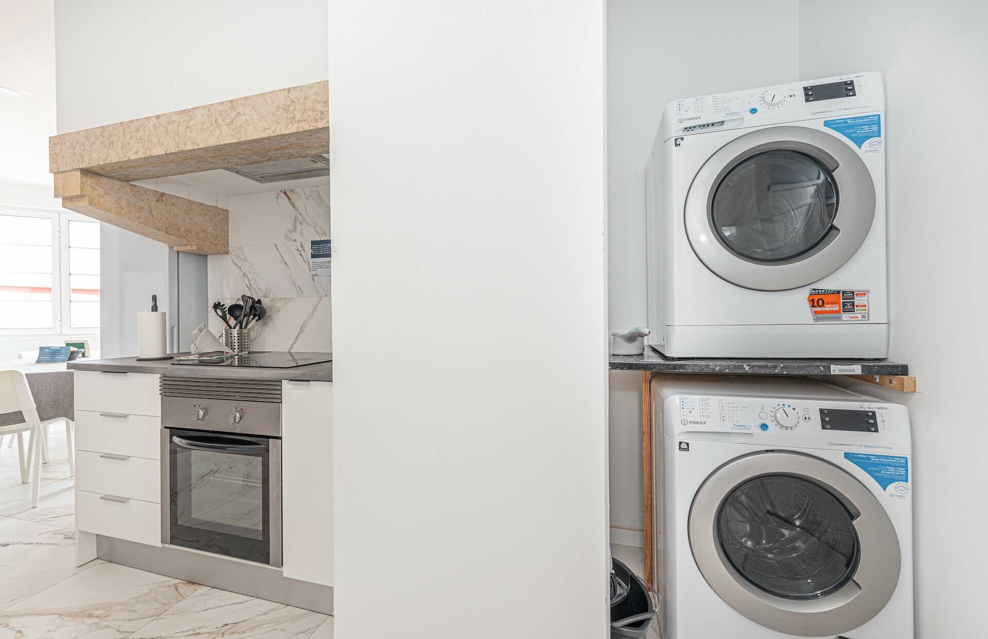 A modern kitchen with a built-in oven, a countertop with kitchen utensils, and a washing machine stacked on top of another appliance.