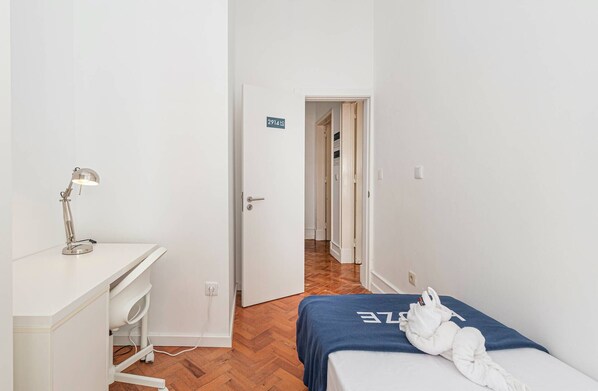 Quarto de hotel com escrivaninha, luminária, cama com toalha e porta que dá para outro quarto.