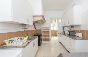 A narrow kitchen with white cabinets, a sink, a stove, and a microwave. - HOUZE Apartment in Historical Lisbon (Lisboa)