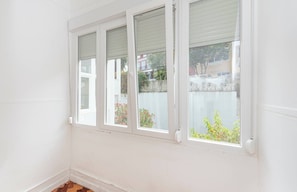 A room with three windows, white walls, and a visible outdoor view with greenery and buildings. - HOUZE Apartment in Historical Lisbon (Lisboa)