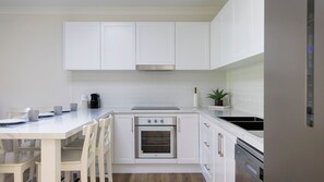 Eine moderne Küche mit weißen Schränken, einem Einbauofen und einer Arbeitsplatte mit Kaffeemaschine und Tassen.