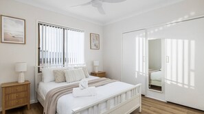Ein Schlafzimmer mit Bett, Nachttischen, einem Spiegel und einem Fenster mit Jalousien.