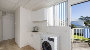 A compact kitchen with a built-in washing machine, a sink, and a window with blinds. - Casa Del Mare  Shoal Bay (Shoal Bay)