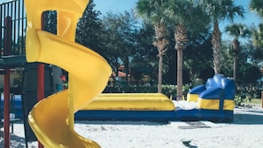 A yellow spiral slide in a park area with palm trees and a blue and yellow inflatable structure. - Family Escape at Holiday Inn Club Vacations Orange Lake (Kissimmee)