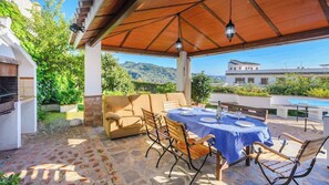 Eine Terrasse im Freien mit Esstisch, einer Sitzecke und einem Grill.