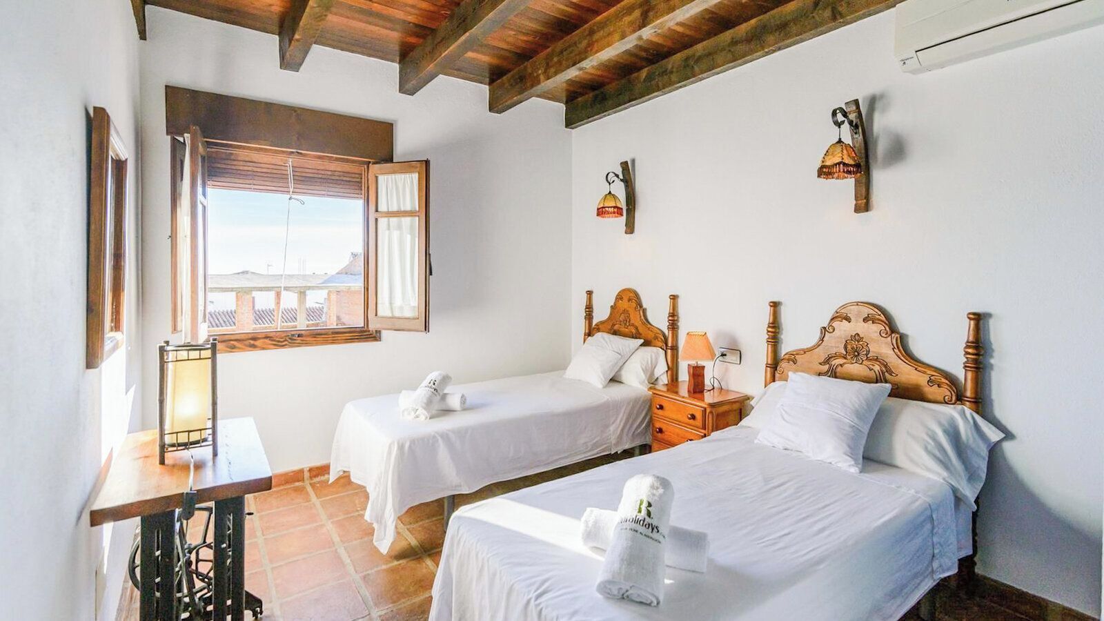 Camera d'albergo con due letti singoli, una testiera in legno, un tavolino con una lampada e una finestra con vista.