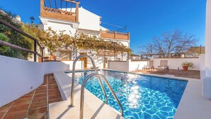 A swimming pool with a metal ladder, a white building with a tiled roof, and a clear blue sky. - Huerta San Francisco Casarabonela by Ruralidays (Málaga)