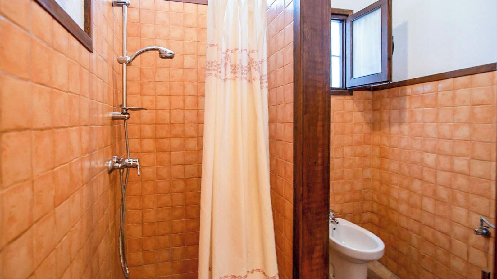 A bathroom with a shower, toilet, and a window above the toilet.
