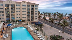 A hotel with a swimming pool, lounge chairs, and a view of the ocean. - Oceanfront 2BR Deluxe at Club Wyndham Oceanside Pier Resort in California (Oceanside)