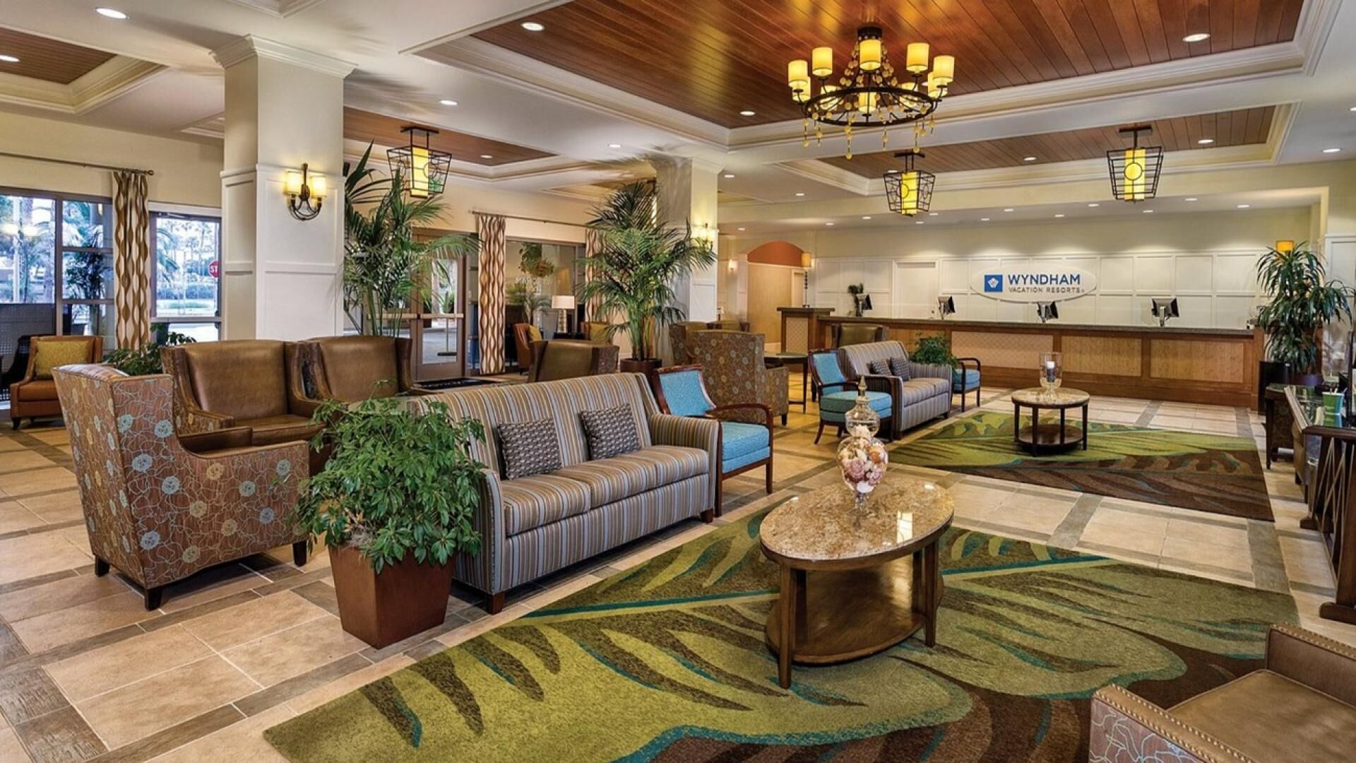 Vestíbulo de hotel con mostrador de recepción, zona de estar con sofás y sillones, y plantas decorativas.