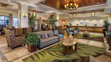 Vestíbulo de hotel con mostrador de recepción, zona de estar con sofás y sillones, y plantas decorativas.