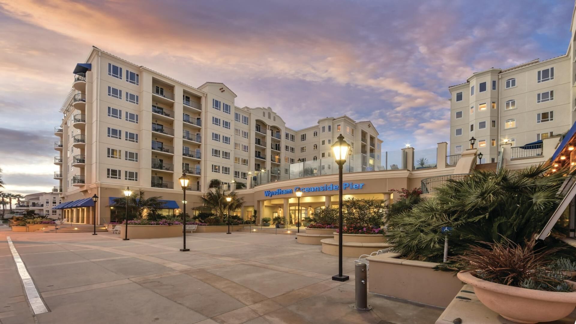 Un hotel con varios pisos, mesas al aire libre y un letrero que dice 'Wyndham Oceanside Pier'.